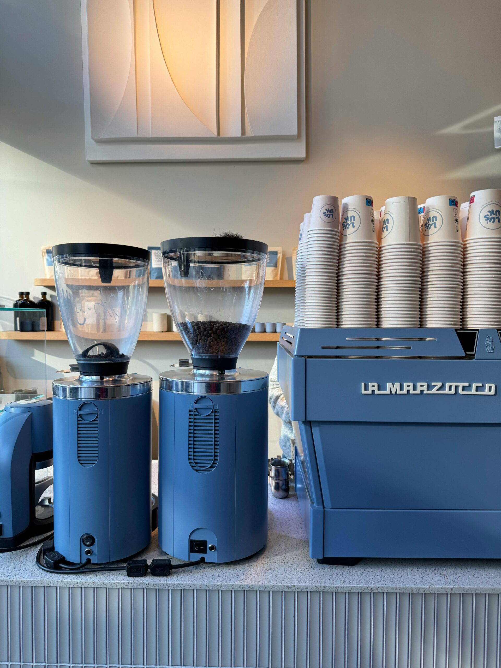 Blue La Marzocco espresso machine and grinders with coffee cups, representing Peak Coffee Techs certified technicians and genuine parts service in Colorado